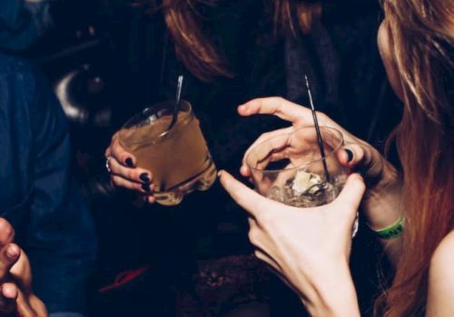 Two people are enjoying drinks and having a conversation in a dimly lit setting, possibly a bar or a party.