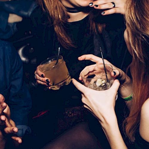 Two people are enjoying drinks and having a conversation in a dimly lit setting, possibly a bar or a party.