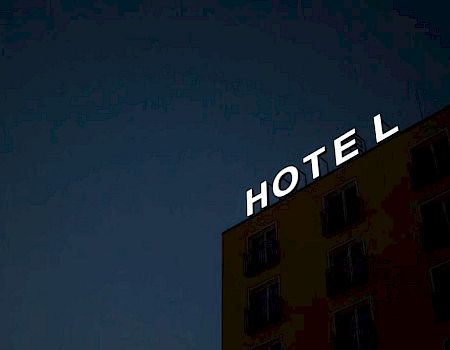 The image shows a nighttime view of a building with a large "HOTEL" sign on its roof, with some letters missing or obscured.
