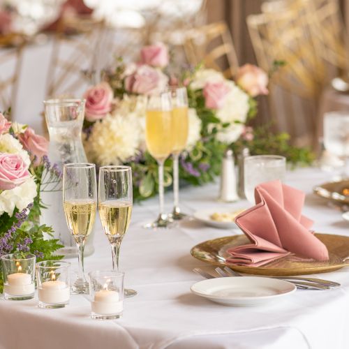 A beautifully set table with elegant floral arrangements, champagne glasses, pink napkins, and candles, perfect for a special occasion.