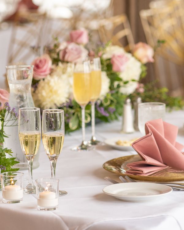 A beautifully set table with elegant floral arrangements, champagne glasses, pink napkins, and candles, perfect for a special occasion.