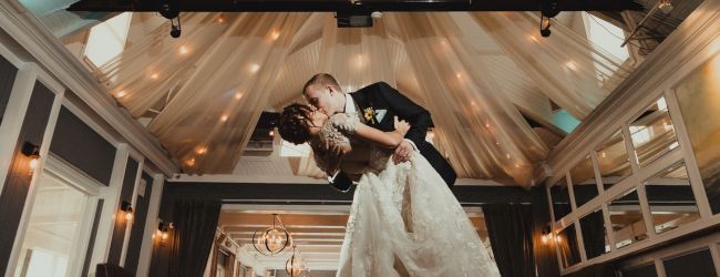 A couple shares a romantic dance in an elegantly decorated venue with draped ceilings and soft lighting.