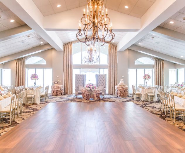 A beautifully decorated banquet hall with chandeliers, round tables set with flowers, elegant chairs, and large windows letting in natural light.