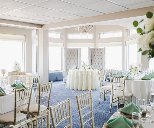 The image shows an elegantly decorated banquet room with round tables, chairs, green napkins, and flower arrangements, set for an event.