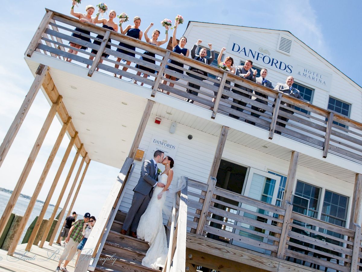 A newlywed couple kisses at the base of a building while their wedding party cheers from the balcony above at Danfords.