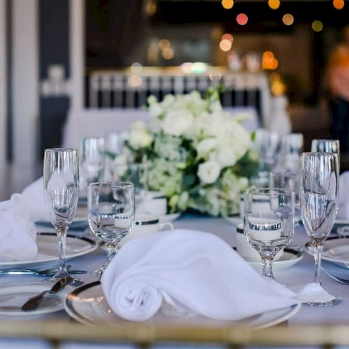 A beautifully set dining table with white napkins, glassware, silverware, and a floral centerpiece, ready for a formal gathering or event.