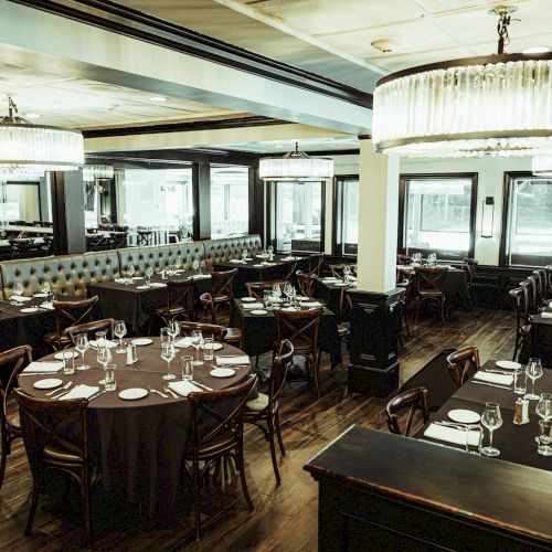 A sophisticated restaurant setting with round and rectangular tables covered in black tablecloths, set with elegant glassware and silverware, ready for guests.