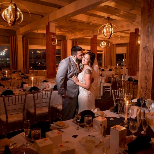 A couple shares a romantic moment in a warmly lit, intricately decorated banquet hall, likely during a wedding reception, surrounded by tables and chairs.