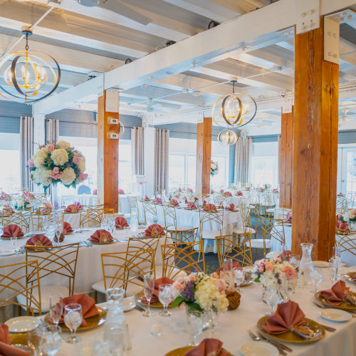 A beautifully decorated banquet hall set up for an event, with arranged tables featuring floral centerpieces, folded napkins, and elegant lighting fixtures.