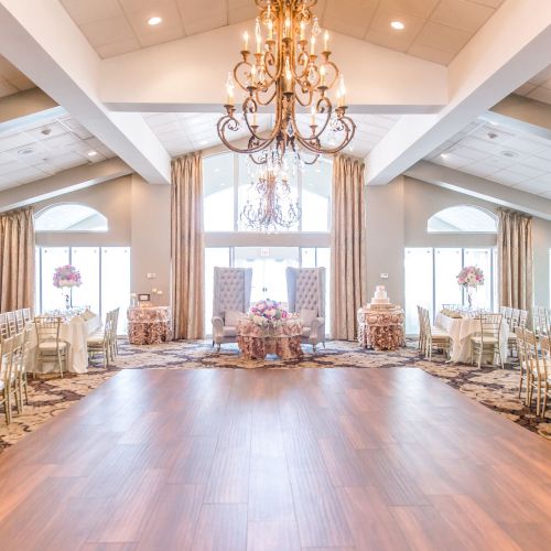 This is an elegant event space with chandeliers, round tables with floral centerpieces, and beige decor, likely set up for a wedding reception.